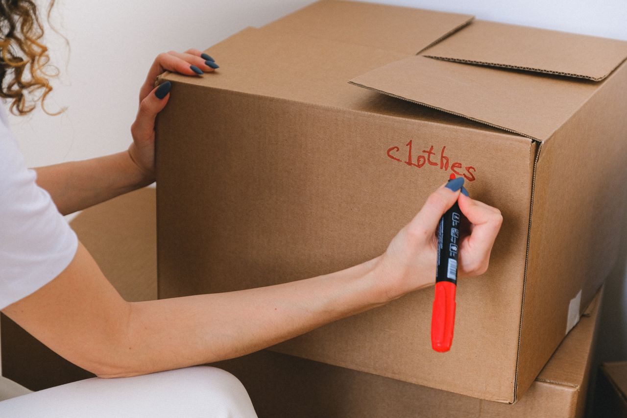 Vue rapprochée d’une femme étiquetant une boîte en carton avec un marqueur rouge à l’intérieur.